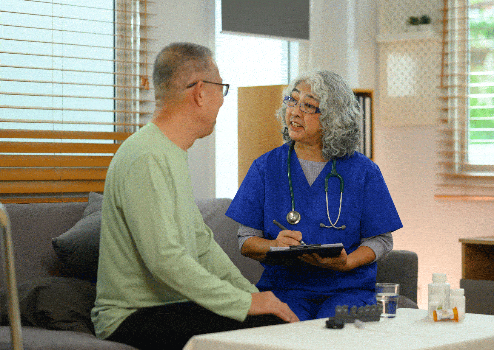 Nurse in scrubs talking to patient on a sofa