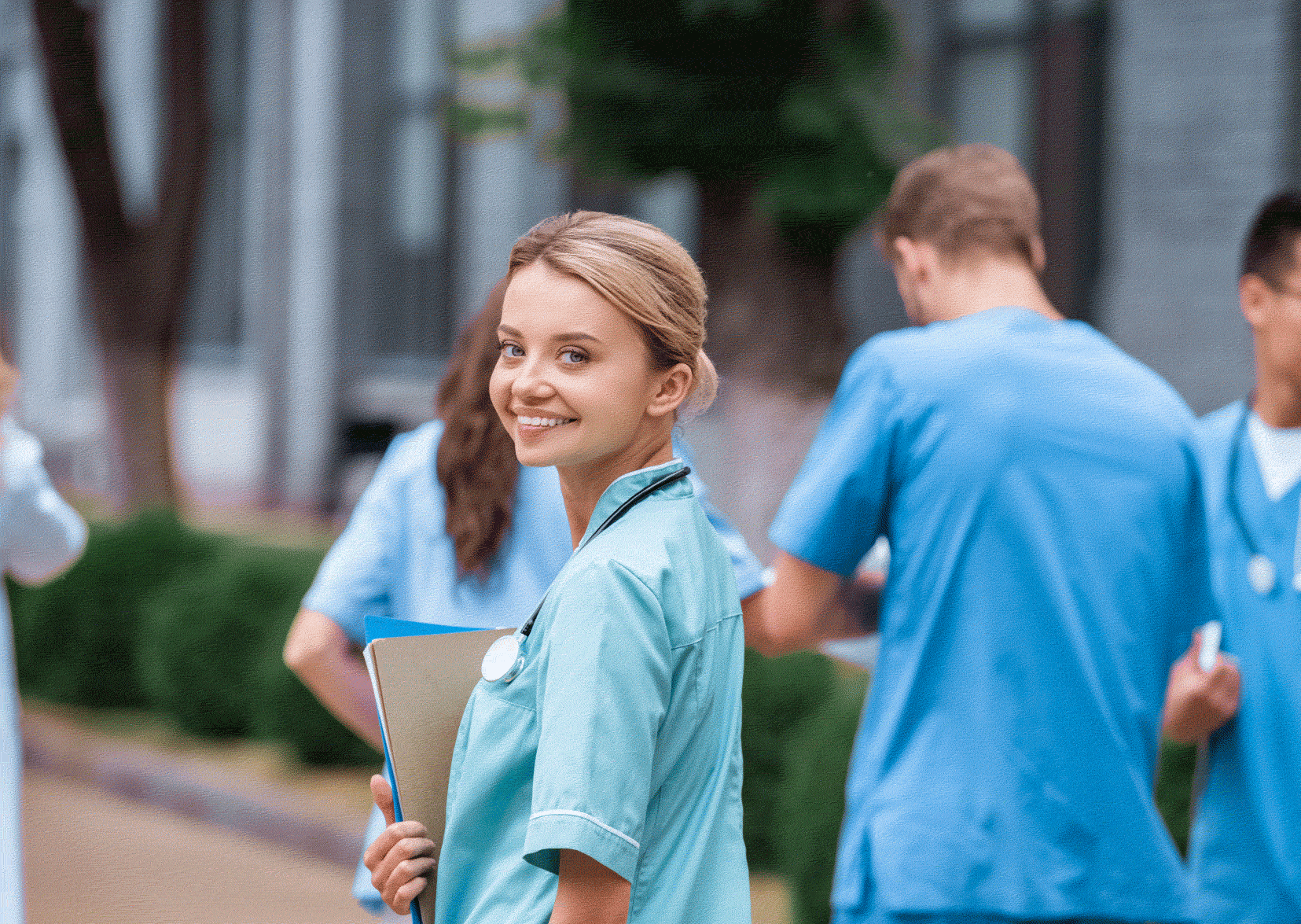 Woman student nurse looking at camera and three male nurses walking in background