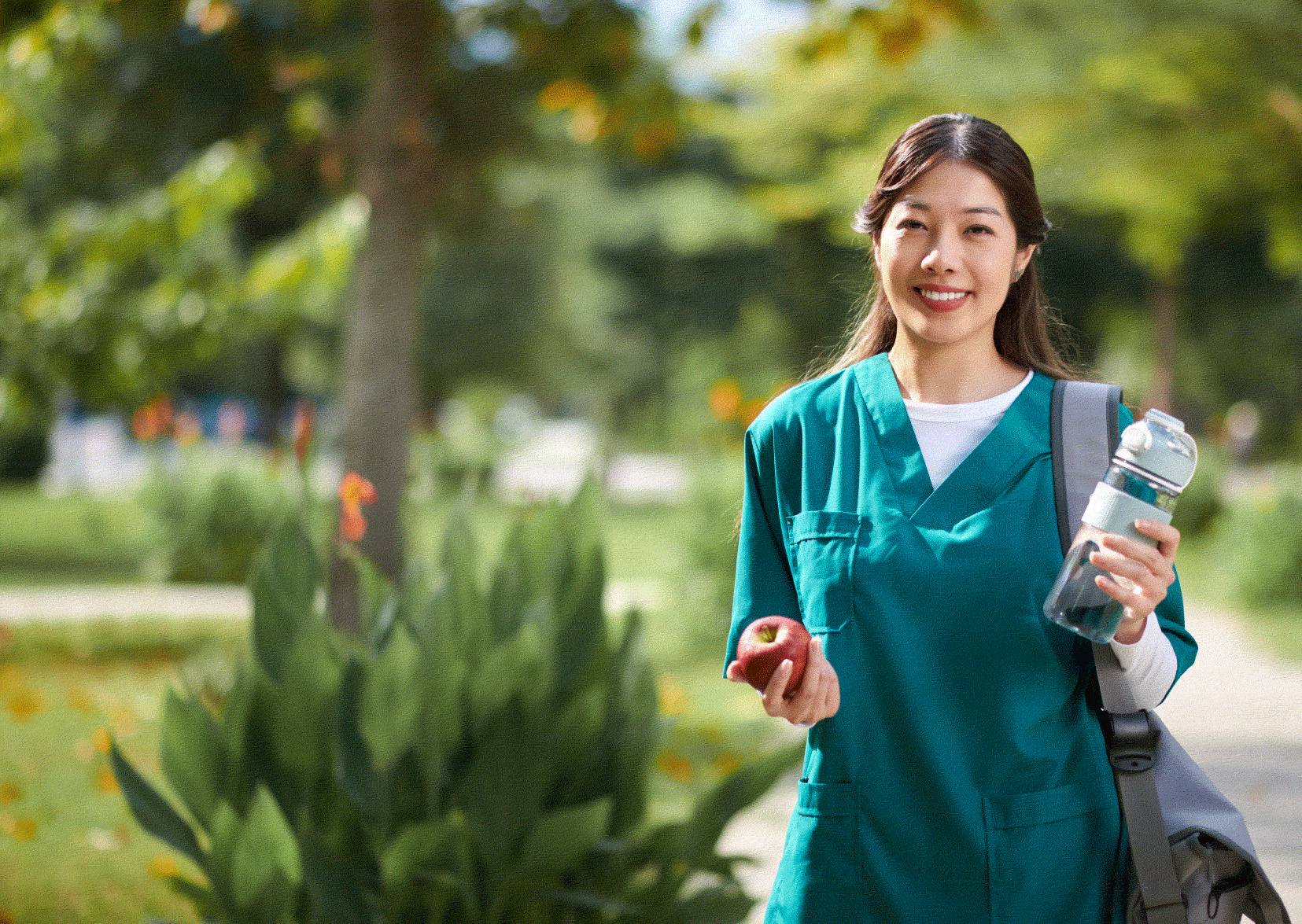 Woman nurse outside in green scrubs smiling with water bottle in her hand